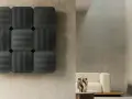 Pannelli neri con righe verticali e orizzontali, che ricordano la convezione termosifone, su una parete grezza. In secondo piano, un divano beige e un tavolino.