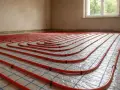 Sistema di riscaldamento a pavimento con tubi rossi disposti a spirale su una griglia blu. L'installazione è pronta per il massetto, garantendo un comfort termico ottimale.