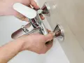 Mani che installano un nuovo miscelatore cromato per la vasca da bagno, parte della sostituzione miscelatore vasca da bagno.