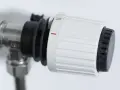 Dettaglio di un detentore termosifone con ghiera bianca e nera, impostato su una tacca intermedia, indica la regolazione della temperatura.