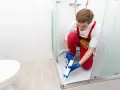 Un operaio con tuta rossa sigilla la fuga tra piatto doccia e piastrelle, prevenendo infiltrazioni d'acqua.