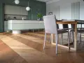 Un elegante parquet a spina di pesce crea un disegno dinamico sotto un tavolo da pranzo e una moderna cucina verde.