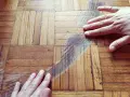 Mani sul parquet rovinato, mostrando graffi e usura. Si valuta come pulire e ripristinare il legno.