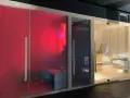 Tre cabine per un'esperienza spa in casa: una rossa con luci LED, una scura e una in legno con sauna tradizionale.