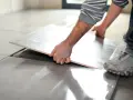 Mano che solleva una piastrella per rimuovere pavimento sovrapposto. Lavori di ristrutturazione in corso.