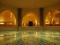 Interno di un bagno dei turchi con piscina e mosaici geometrici. Archi moreschi e colonne decorate creano un'atmosfera orientale.
