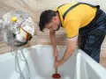 Uomo con sturalavandini prova a sturare la vasca da bagno. In un cerchio, bicarbonato e aceto, rimedi naturali per sturare la vasca da bagno.