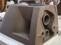 A brown ceramic toilet tank mold with visible pipes and openings, in a workshop setting.