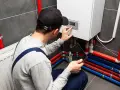 Uomo con tablet e cappellino esegue pulizia impianto riscaldamento fai da te, controllando la caldaia e i tubi colorati.