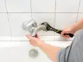 Mano con chiave inglese ripara un rubinetto che perde dal miscelatore, sopra la vasca da bagno.