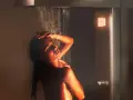 Donna sotto una doccia emozionale, illuminata da luci calde, con acqua che scorre sul suo corpo.