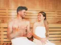 Coppia sorridente in una sauna di legno, un rituale di benessere quotidiano.