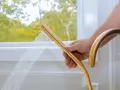 Mano che tiene un soffione doccia dorato, con acqua che scorre. Un esempio pratico su come pulire il tubo flessibile della doccia per un getto ottimale.