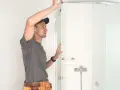 Installazione di un montaggio box doccia rettangolare. Un operaio con cintura degli attrezzi sistema il vetro.