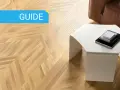 Guida: parquet spazzolato pro e contro. Pavimento in legno con motivo a spina di pesce, tavolino bianco e divano in pelle marrone.