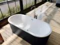 Vasca da bagno freestanding nera con rubinetteria cromata. Le misure della vasca da bagno sono ideali per un bagno moderno con vista sul giardino.