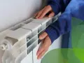 Mani che toccano un termosifone bianco, suggerendo come svuotare termosifone per la manutenzione.