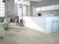Cucina moderna con isola bianca, divano e pavimenti in legno chiaro. Quanti pavimenti si possono sovrapporre per creare questo look?