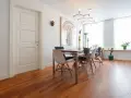 Un elegante soggiorno con parquet doussié e arredamento moderno. Tavolo da pranzo con sedie di design, quadro astratto e lampadario geometrico.