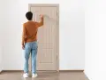 Uomo con maglione arancione e jeans bussa alla porta, forse per alzare la porta per posa pavimento.