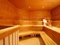 Donna rilassata in una sauna a 90 gradi, avvolta in un asciugamano bianco, circondata dal calore del legno.