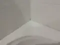 Angolo di una vasca da bagno con piastrelle bagnate e un sigillante bianco appena applicato per sigillare la vasca da bagno.