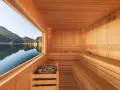 Interno di una sauna in legno con vista su un lago e montagne. Un luogo perfetto per capire cos'è una spa: relax e natura.