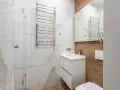 Bagno moderno con termoarredi cromati, lavabo sospeso e rivestimenti in marmo e legno.