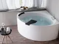 Una vasca da bagno angolare bianca, piena d'acqua, con accessori da bagno e un fiore su un tavolino. Un'esperienza novellini divina.