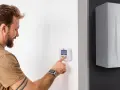 Uomo interagisce con termostato digitale, mostrando la differenza tra termostato e cronotermostato per ottimizzare il riscaldamento.