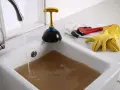 Acqua sporca ristagna in un lavandino bagno otturato. Attrezzi per lo spurgo: sturalavandini, chiave inglese e guanti gialli.