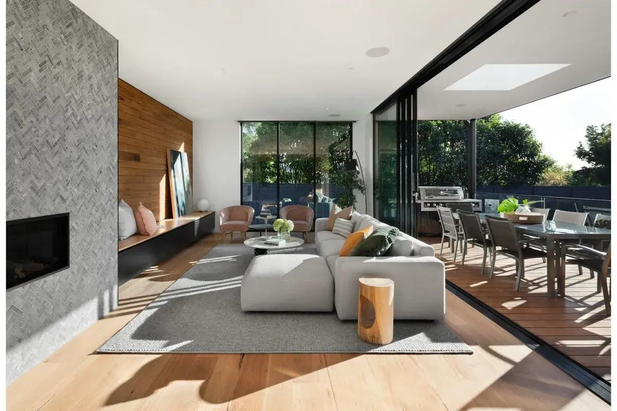 Soggiorno moderno con camino in pietra, divano bianco, e un bellissimo parquet essenze che si estende verso l'esterno, collegandosi alla zona pranzo esterna.