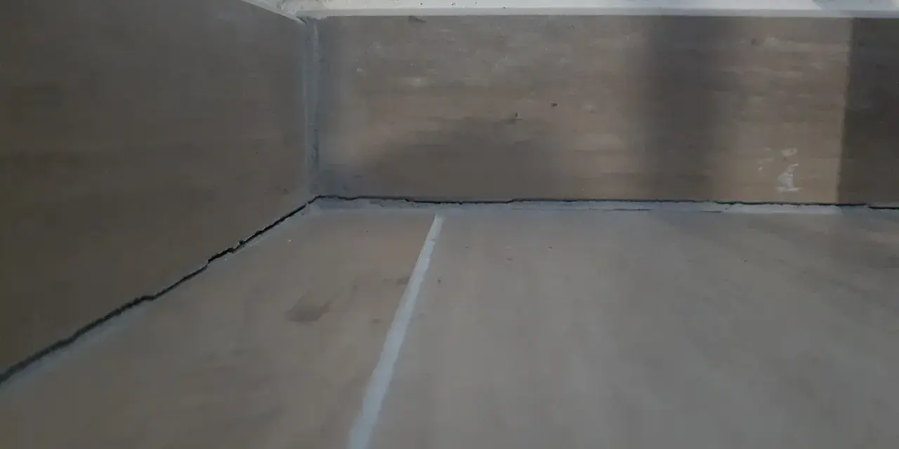 Angolo di una stanza con pavimento in legno e battiscopa. Si vedono le crepe tra il battiscopa e il muro, un dettaglio da considerare dopo il massetto.