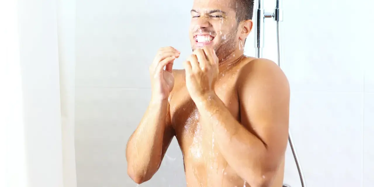 Uomo sotto la doccia dopo allenamento, con acqua che gli scorre sul viso e sul corpo.