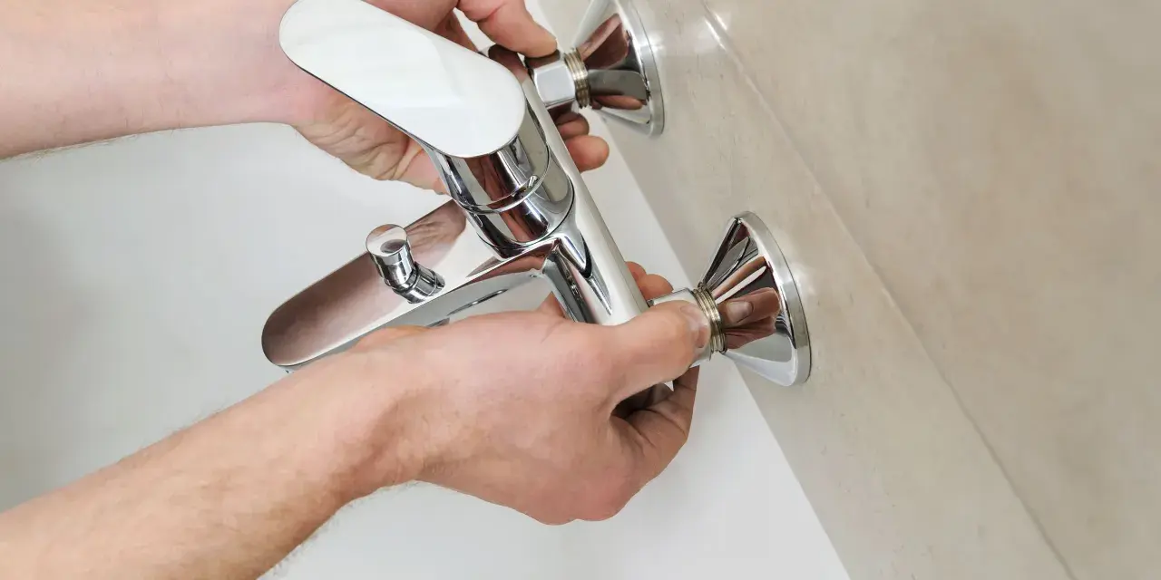 Mani che installano un nuovo miscelatore cromato per la vasca da bagno, parte della sostituzione miscelatore vasca da bagno.