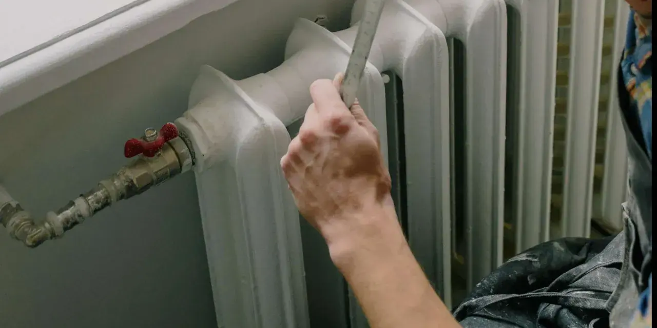 Mano con righello vicino a termosifone, pronto a cambiare valvola termostatica senza svuotare impianto.
