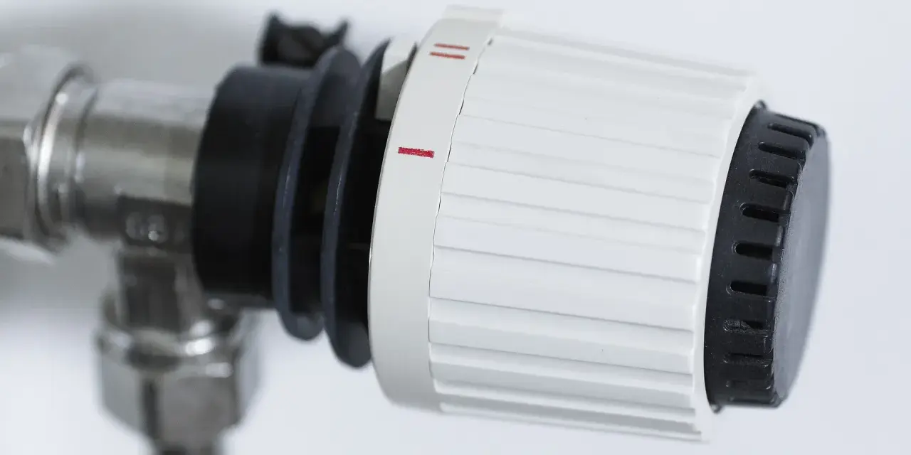 Dettaglio di un detentore termosifone con ghiera bianca e nera, impostato su una tacca intermedia, indica la regolazione della temperatura.