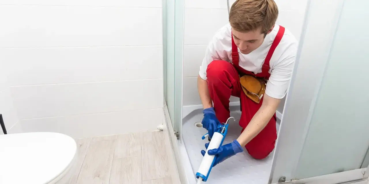 Un operaio con tuta rossa sigilla la fuga tra piatto doccia e piastrelle, prevenendo infiltrazioni d'acqua.