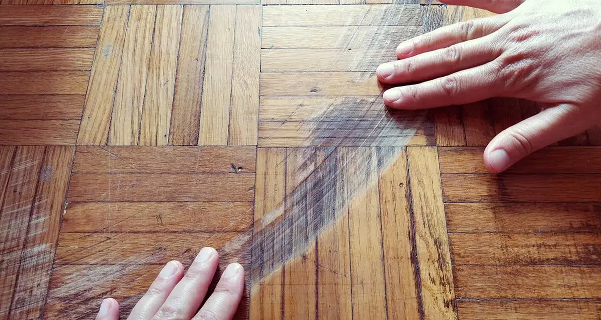 Mani sul parquet rovinato, mostrando graffi e usura. Si valuta come pulire e ripristinare il legno.