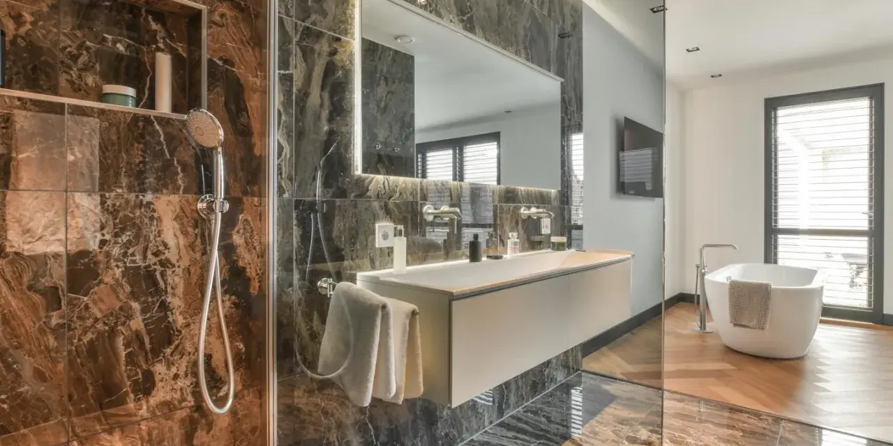 Bagno di lusso con doccia e vasca. Rubinetteria Bossini cromata, lavabo sospeso e specchio illuminato. Marmo scuro e parquet.