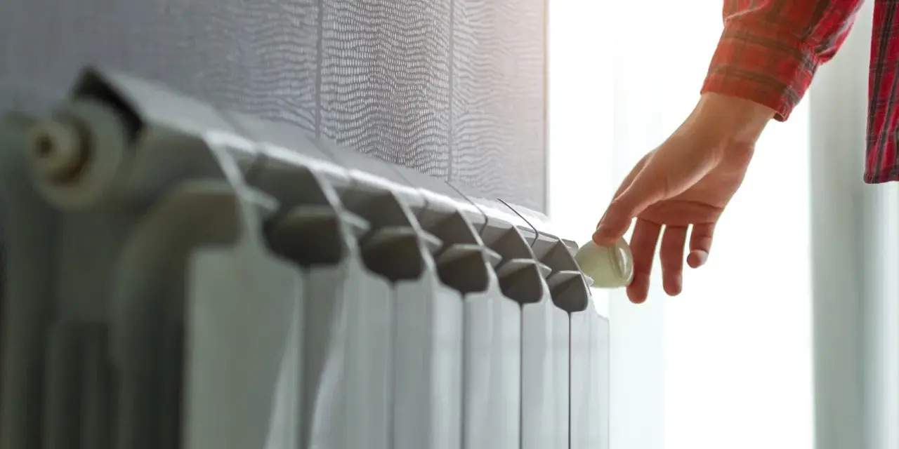Mano che regola la valvola di un termosifone. Scopri quanto costa cambiare i termosifoni per un riscaldamento efficiente.