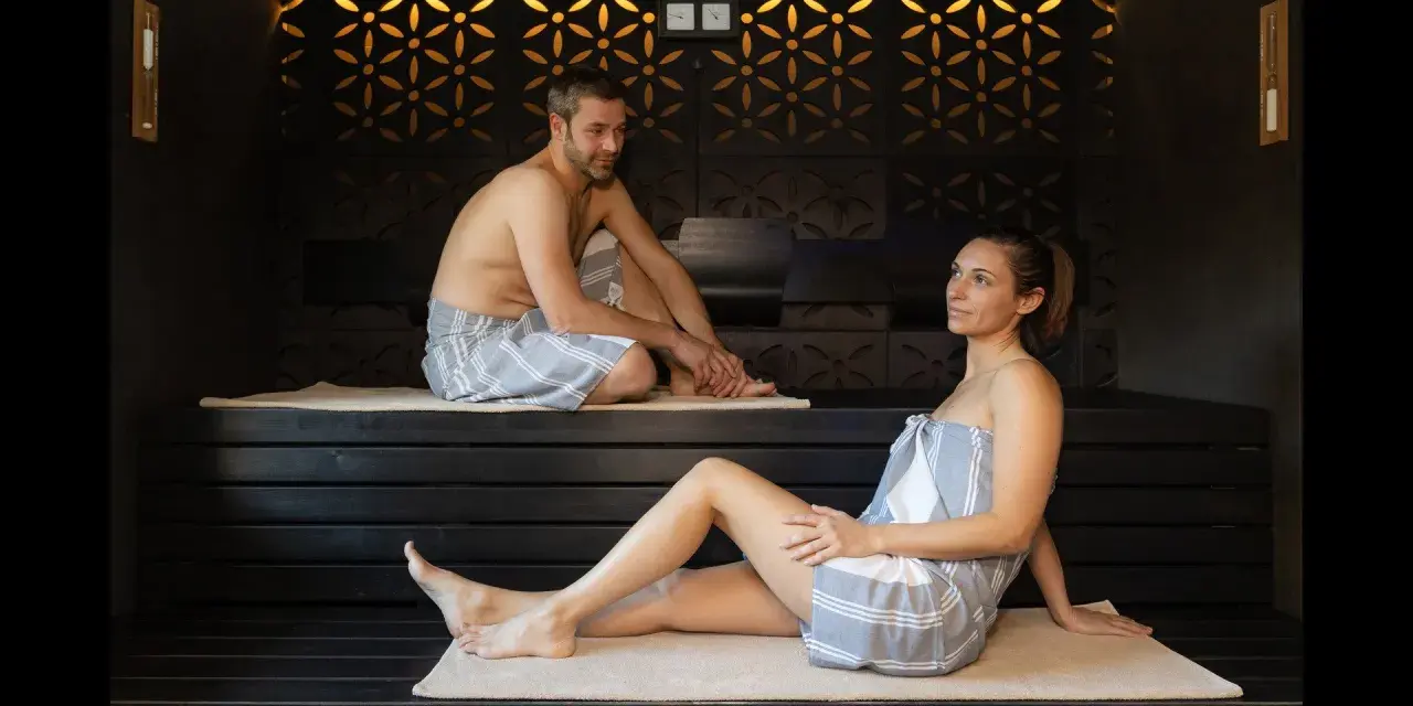 Coppia rilassata in un bagno turco, con clessidra per misurare il bagno turco quanto tempo.