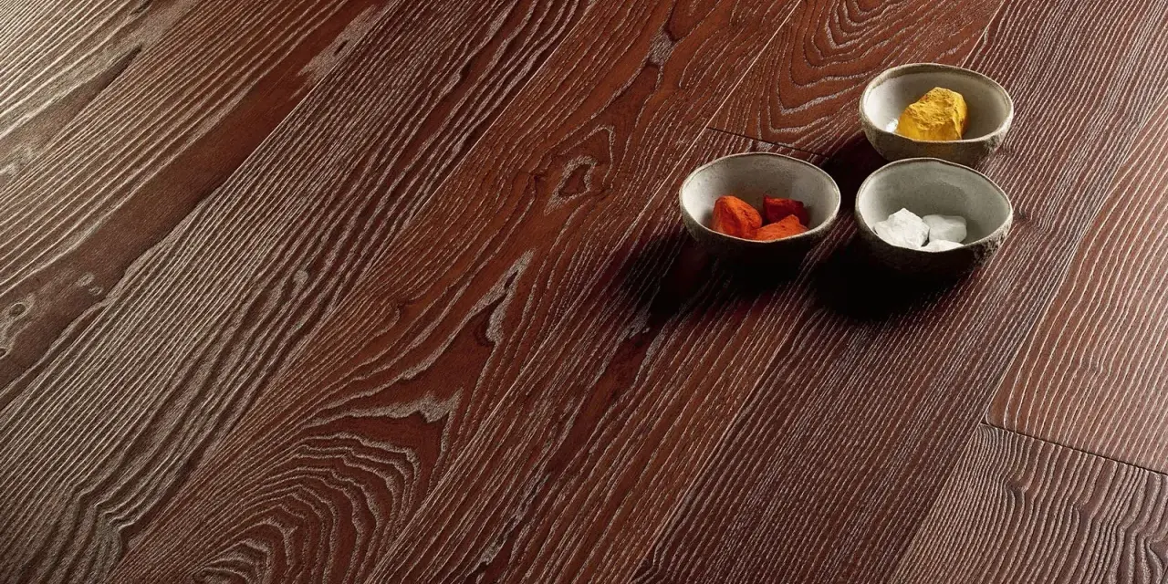 Superficie in parquet massello o prefinito con venature marcate. Tre ciotoline con elementi decorativi colorati.