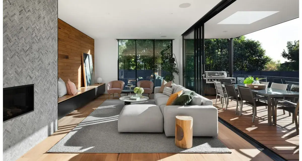 Soggiorno moderno con camino in pietra, divano bianco, e un bellissimo parquet essenze che si estende verso l'esterno, collegandosi alla zona pranzo esterna.