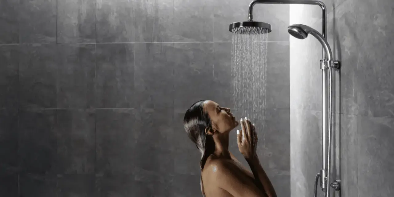 Donna sotto una doccia walk in dimensioni ideali, con le mani giunte sotto il getto d'acqua.