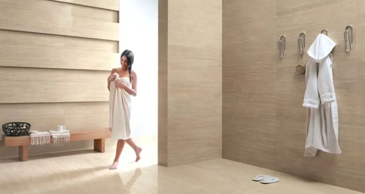 Bagni moderni con donna avvolta in un asciugamano, accappatoio appeso e panchina in legno.