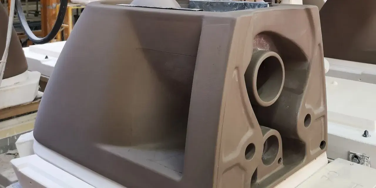A brown ceramic toilet tank mold with visible pipes and openings, in a workshop setting.