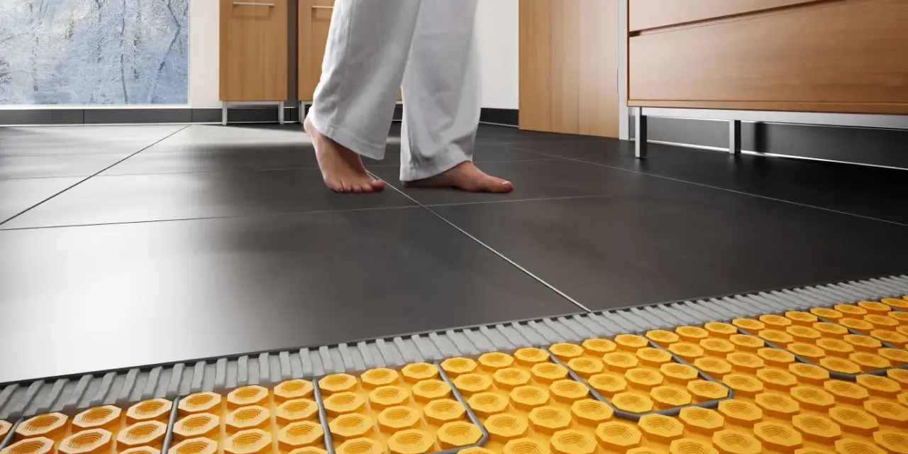 Piedi nudi su pavimento scuro, con sistema di riscaldamento a pavimento su pavimento esistente visibile sotto.