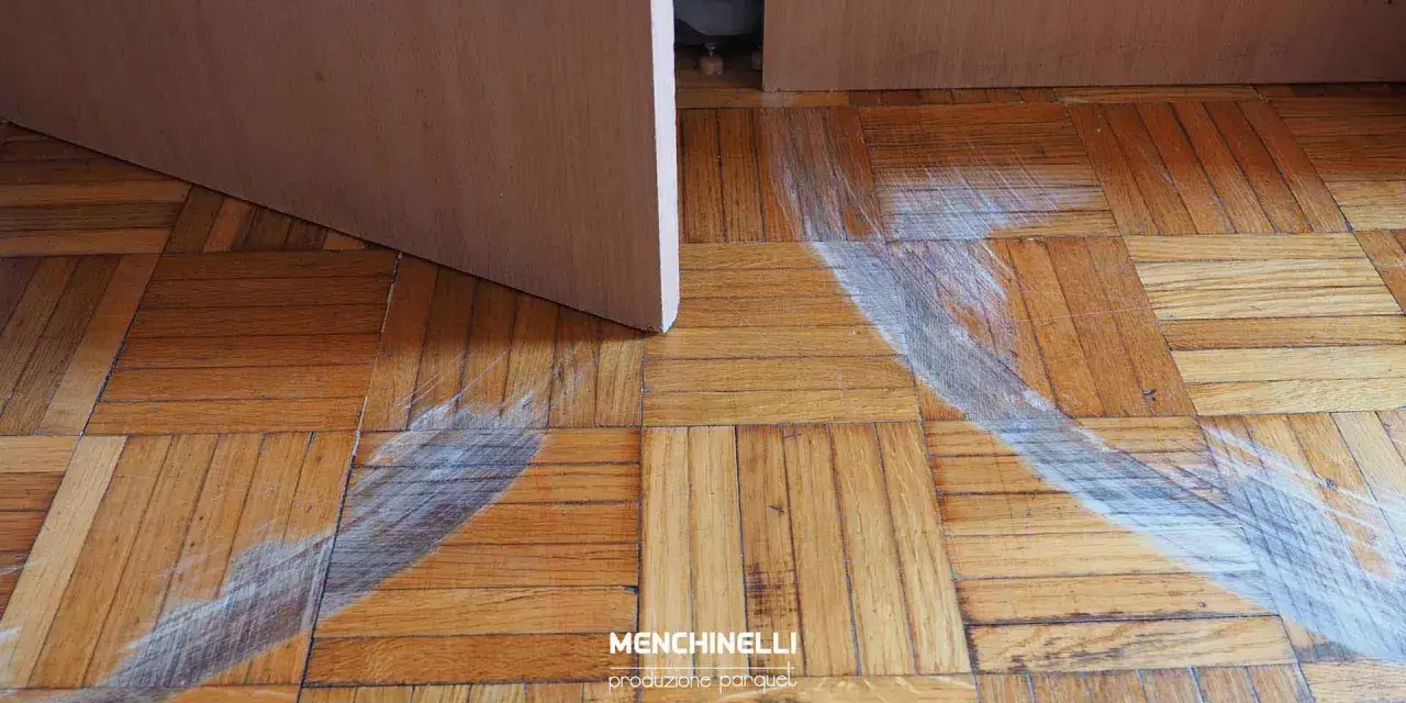 Rimozione di parquet incollato con segni di usura sul pavimento in legno.