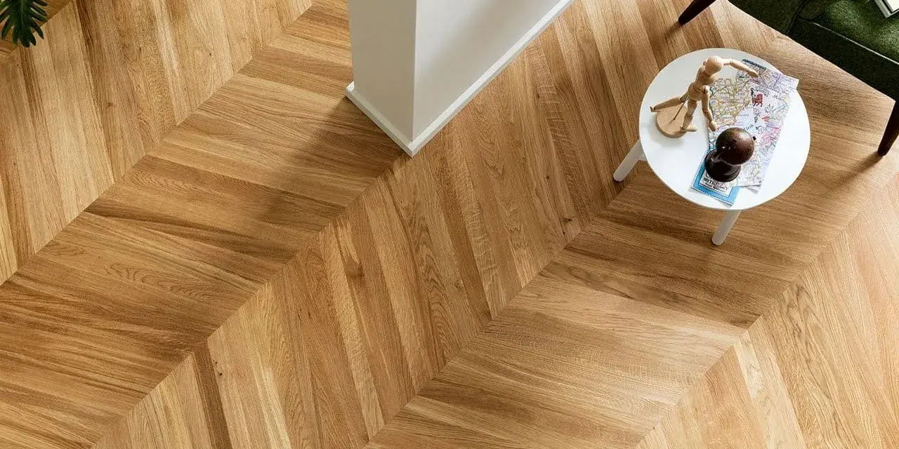 Un elegante parquet oliato a spina di pesce, con un tavolino bianco e una poltrona verde. Scopri come pulire il tuo parquet oliato per mantenerlo splendente.